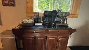 Une cuisine équipée d’une machine à café, de sucre, de thé et de récipients contenant du café, le tout posé sur le comptoir.