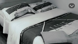 Un lit avec une couette blanche et plusieurs oreillers, dont certains sont ornés de motifs ou d’inscriptions.