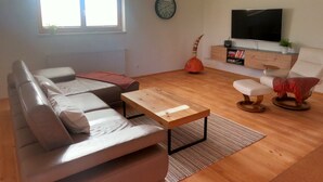Uma sala de estar com sofá, mesa de centro, televisão e estante de livros.