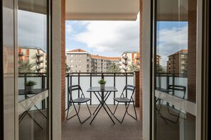 A balcony with two tables and chairs, a potted plant, and a view of surrounding buildings. - Relax Urbano con Balcone | Metro e San Siro (Milano)