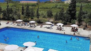 A swimming pool with lounge chairs and umbrellas, surrounded by greenery and buildings in the background. - Big Seaview studio, 24h electricity, beach + pool (Jabal Lubnan)