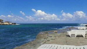 A beach with white lounge chairs and a concrete walkway. - Nonstop electricity 1 bedroom beachfront apartment (Jabal Lubnan)
