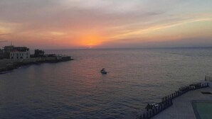 A coastal sunset view with a pier and a boat on the water. - Nonstop electricity 1 bedroom beachfront apartment (Jabal Lubnan)