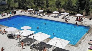 A swimming pool with lounge chairs and umbrellas, surrounded by greenery and buildings. - Nonstop electricity 1 bedroom beachfront apartment (Jabal Lubnan)