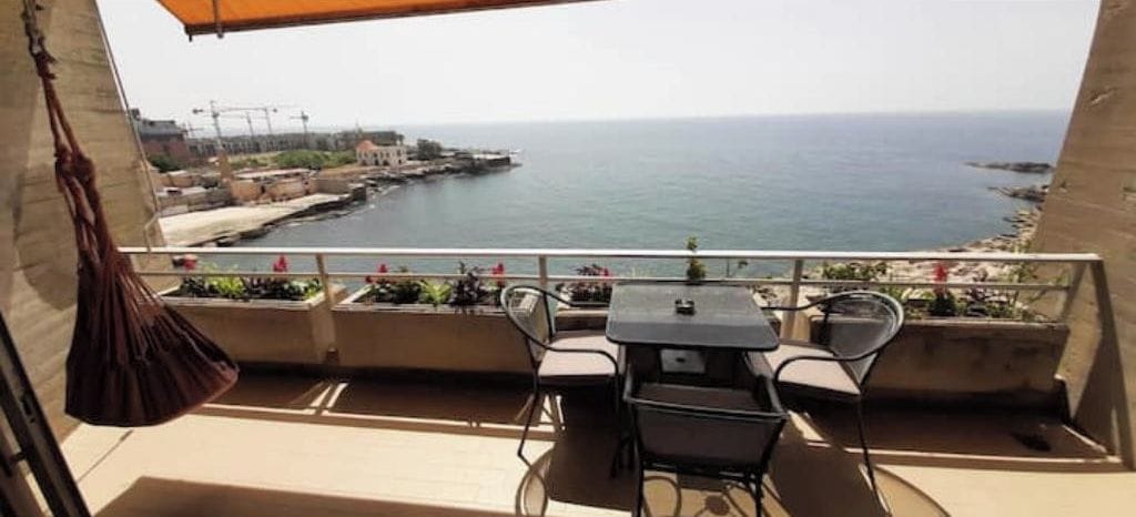 Un balcón con mesa y sillas, con vistas a la costa y al mar, con una línea de costa distante.