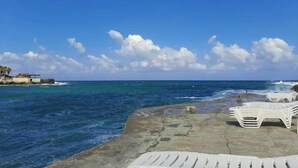 A beach with white lounge chairs and a concrete walkway along the shore.