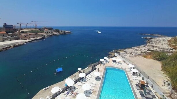 A coastal hotel with a swimming pool, lounge chairs, and a view of the sea.