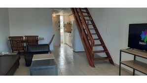 A living room with a sofa, a coffee table, a TV on a stand, a wooden ladder, and a kitchen in the background. - Family Duplex, beach+pool access (Jabal Lubnan)