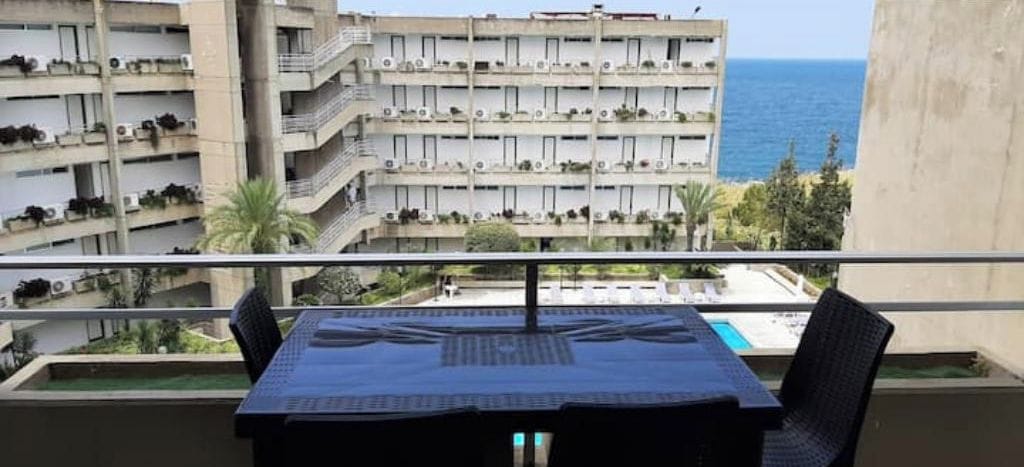 Un balcón con mesa y sillas, con vistas a una piscina y un edificio con varios balcones.
