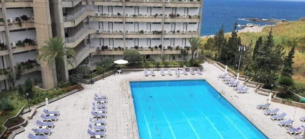 A hotel pool with sun loungers and a view of the sea.