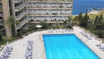 A hotel pool with sun loungers and a view of the sea.