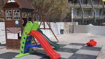A playground with a slide and a small wooden structure with a clock.