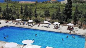 A swimming pool with lounge chairs and umbrellas, surrounded by greenery and buildings in the background. - Family Duplex, beach+pool access (Jabal Lubnan)