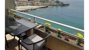A balcony with a table and chairs overlooking a coastal area with buildings and a pier. - 24/7 electricity Seaview studio with beach access (Jabal Lubnan)