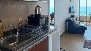 A compact kitchen with a sink, stove, and cabinets. A small refrigerator is visible. The room has a view of the ocean through large windows. - 24/7 electricity Seaview studio with beach access (Jabal Lubnan)