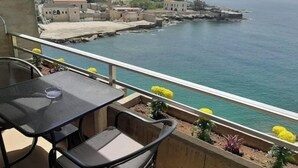 A balcony with a table and chairs overlooking a coastal area with buildings and a pier. - 24/7 electricity Seaview studio with beach access (Jabal Lubnan)