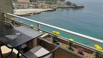 A balcony with a table and chairs overlooking a coastal area with buildings and a pier.