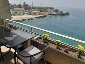 A balcony with a table and chairs overlooking a coastal area with buildings and a pier. - 24/7 electricity Seaview studio with beach access (Jabal Lubnan)