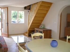 Un coin repas avec une table à plateau de verre, un vase bleu et un escalier en bois.