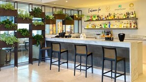 Zona de bar moderna con una barra central, taburetes y una pared con estantes llenos de botellas.
