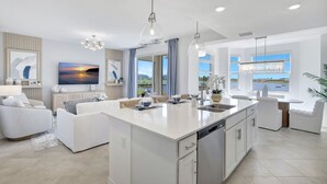 Una cocina moderna con una isla central, un comedor con una mesa redonda y una sala de estar con un sofá y un cuadro.