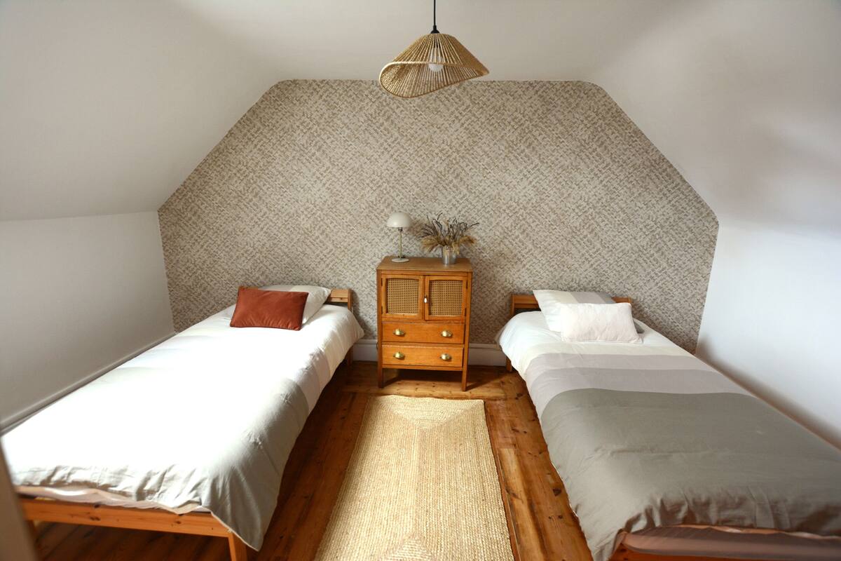 A bedroom with two single beds, a wooden dresser, a woven rug, and a textured wall.