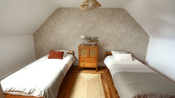 Un dormitorio con dos camas individuales, un aparador de madera, un tapete tejido y una pared con textura.
