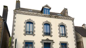 A two-story building with a blue door and windows, featuring a symmetrical facade and stone detailing. - Les Suites Fisel (Rostrenen)