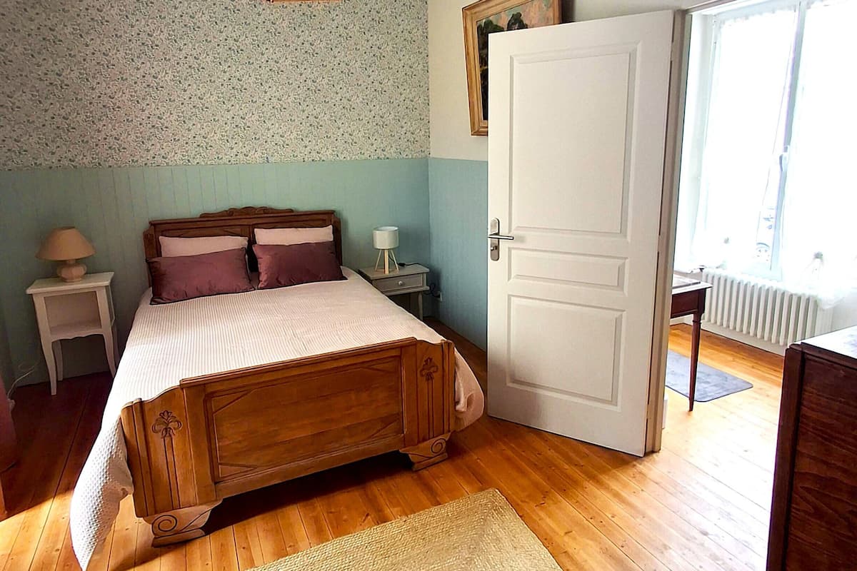 A bedroom with a wooden bed, a hanging light fixture, a door, and a view of the outside.