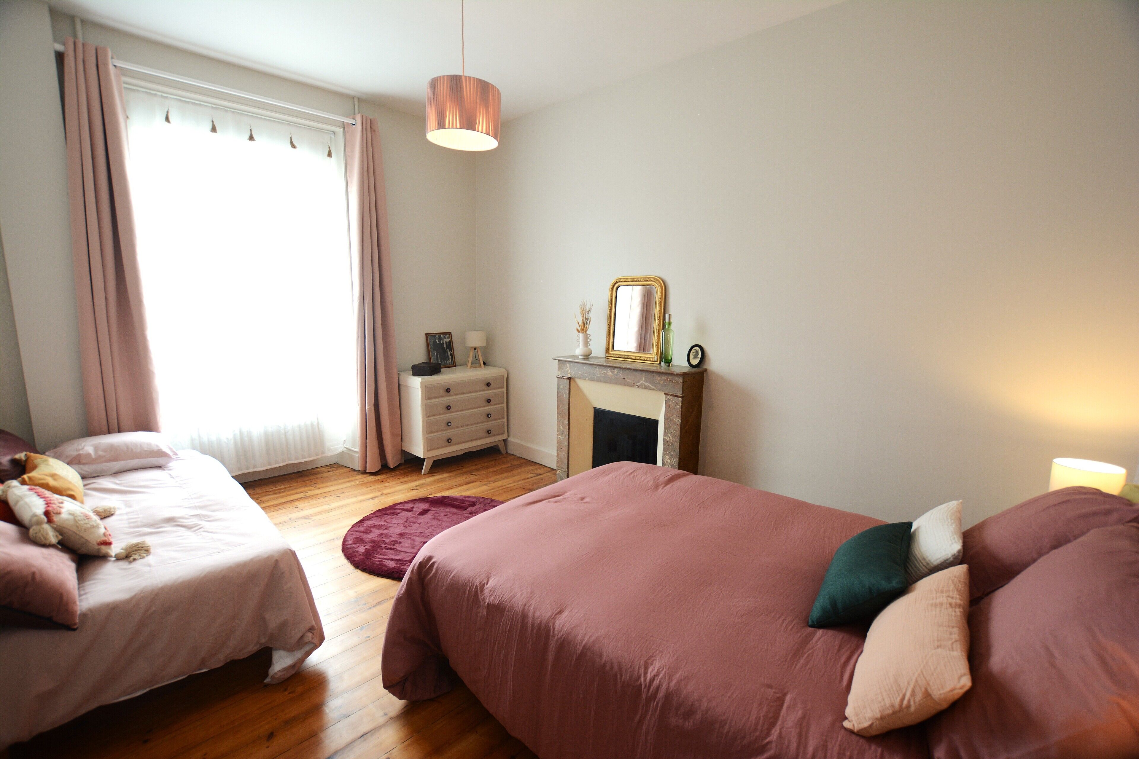 Une chambre avec deux lits, une commode, un miroir et une cheminée.