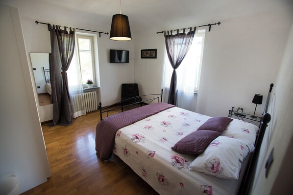 A bedroom with a bed, curtains, a radiator, a mirror, and a window.