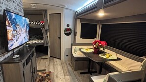 Un intérieur de camping-car accueillant, avec un téléviseur, des lits superposés, un coin repas et une pancarte « Bienvenue ».