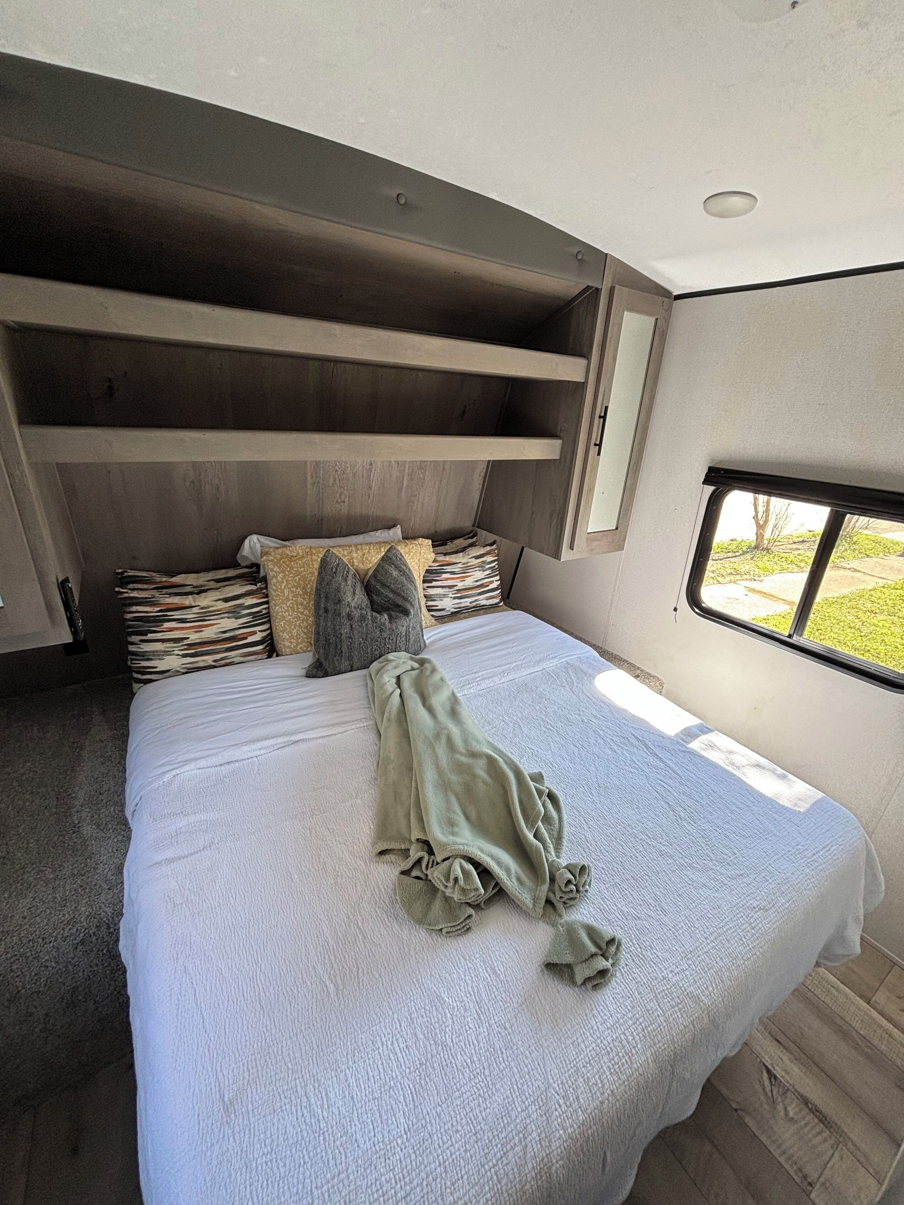 A bedroom with a bed, pillows, a blanket, built-in shelves, and a window.