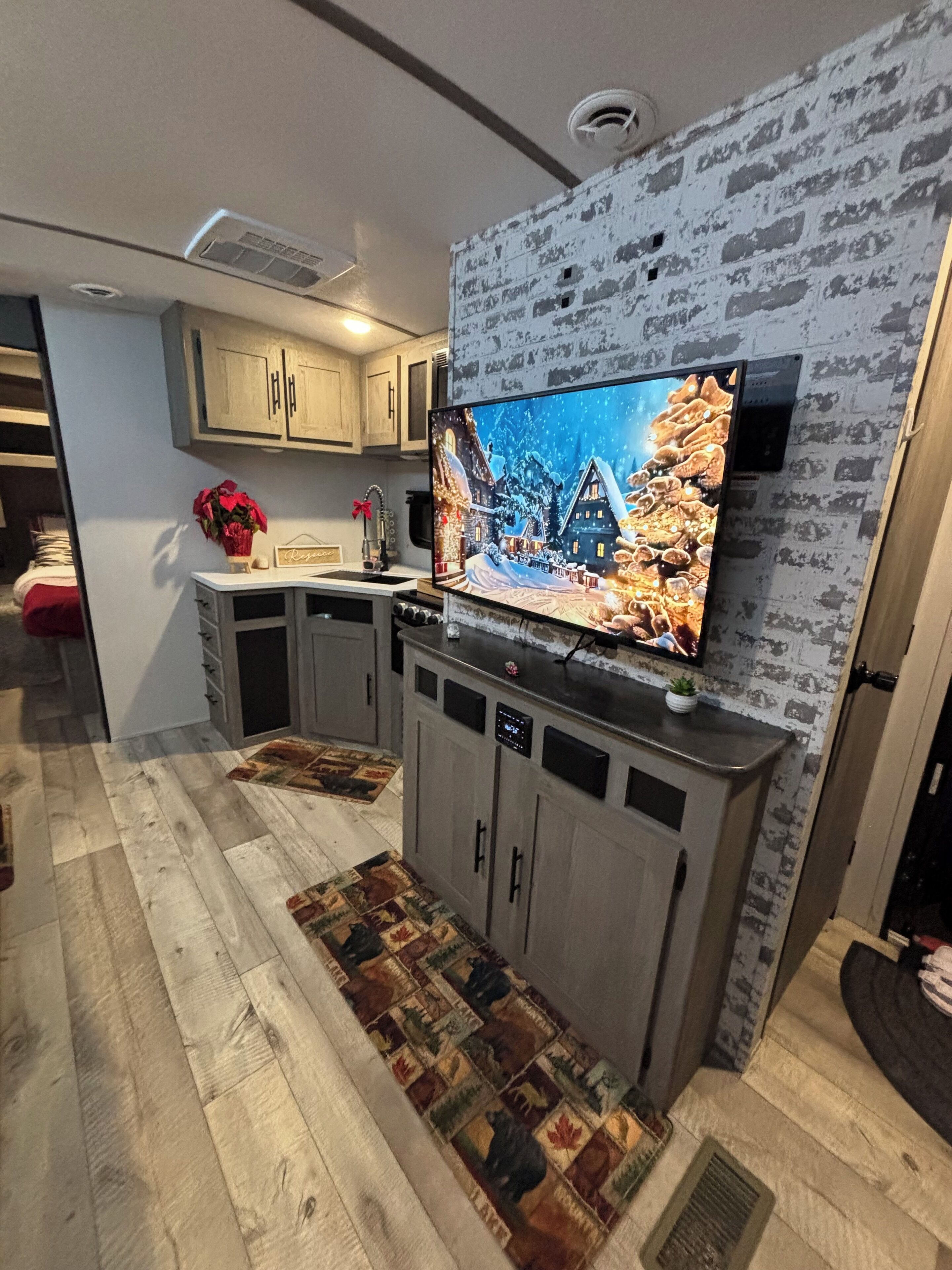 Une cuisine moderne avec un grand téléviseur à écran plat fixé à un mur texturé, des armoires en bois et un tapis à motifs.