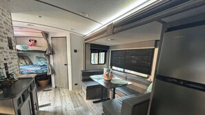 Une cuisine compacte pour camping-car, équipée d’un réfrigérateur, d’une table à manger et d’un petit coin salon.