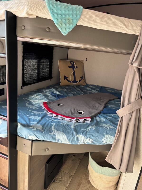 A bunk bed with a blue dinosaur-themed mattress, a beige pillow with an anchor design, and a small window with a mesh screen. - Cozy RV in Serene Dallas with AC
with a private room and 2 bunk beds plus one (Dallas)
