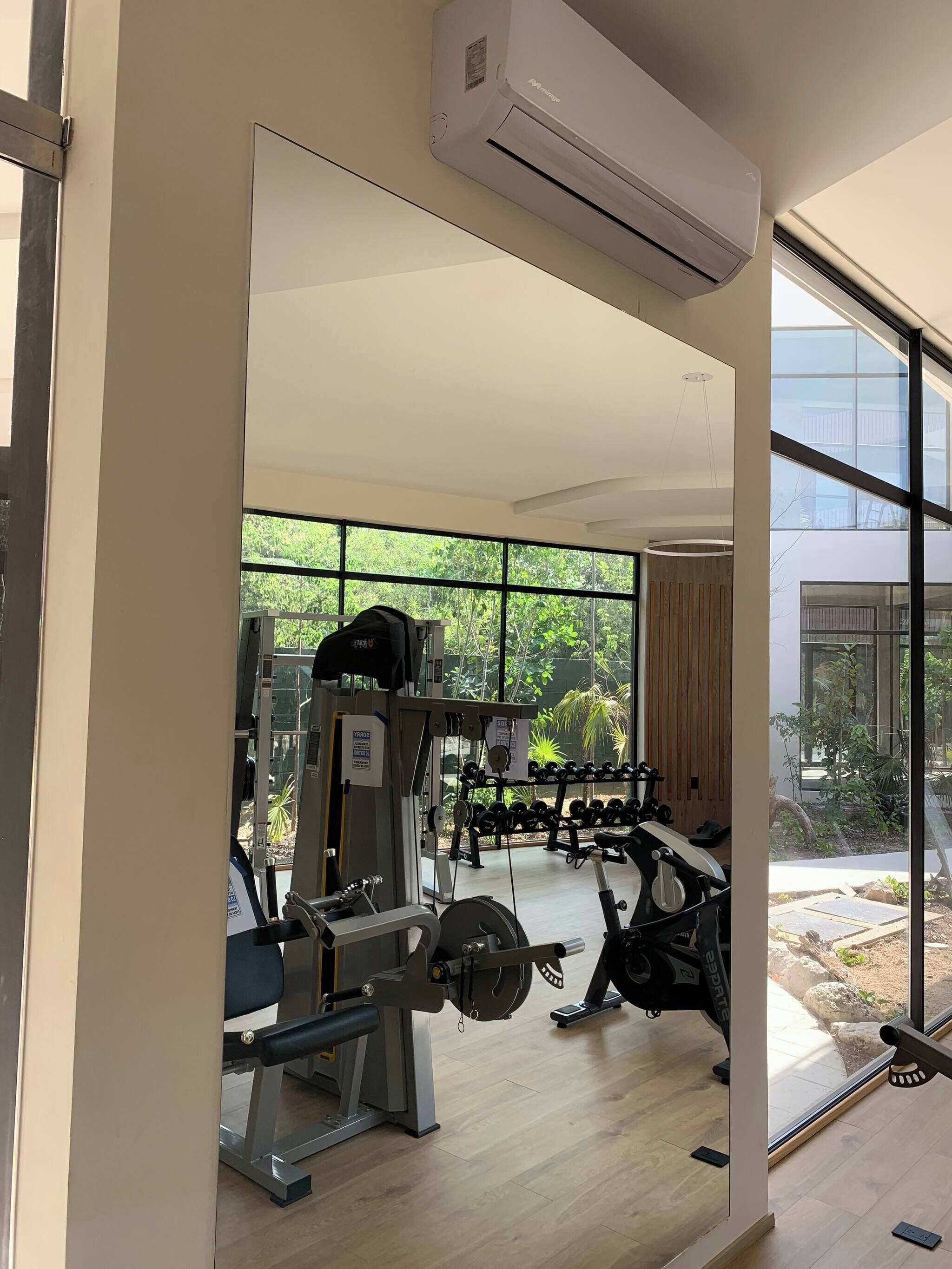Ein Fitnessraum mit unterschiedlichen Trainingsgeräten, großen Fenstern und einer Klimaanlage.