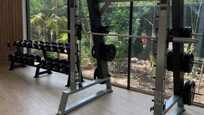 A gym with weightlifting equipment and large windows offering a view of greenery. - Unique Rooftop Sea View Walking to Beach The Best (Tulum)