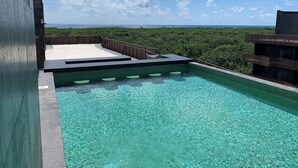 A rooftop pool with clear blue water, surrounded by lush greenery and a view of the ocean. - Unique Rooftop Sea View Walking to Beach The Best (Tulum)