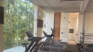 A gym with stationary bikes and a bench press area, large windows, and a view of trees. - ¡PH 3 Quarts Terrace and Private Pool AZ Premium! (Tulum)