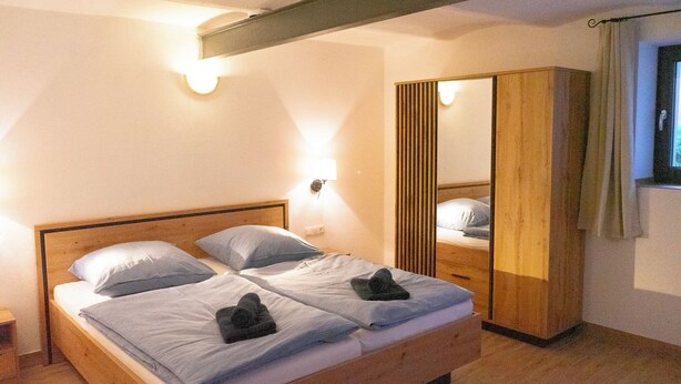 Una cama doble con dos almohadas y una colcha, un armario de madera y un espejo.