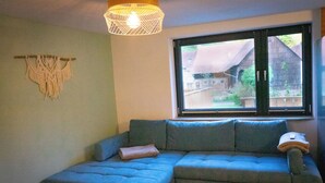 Una habitación con un sofá azul, un tapiz de macramé y una ventana con vistas a edificios.