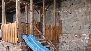 Un tobogán azul en un ambiente rústico interior con vigas de madera y paredes de ladrillo.