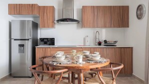A compact kitchen with wooden cabinets, a stainless steel refrigerator, a microwave, and a dining table set with plates and cups. - Beautiful and Comfortable, 1 Bedroom! The Best in Zama! (Tulum)