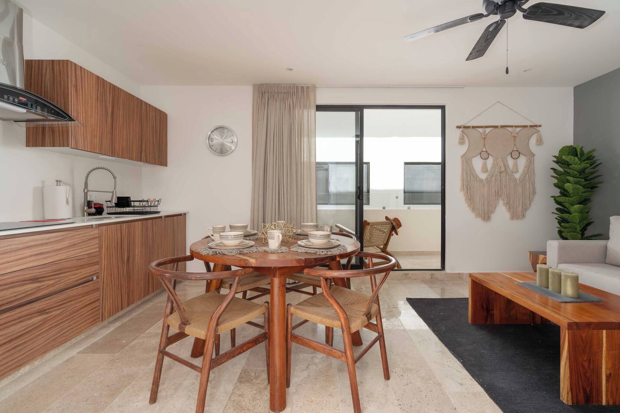 Une cuisine moderne avec des meubles en bois, une table à manger avec des chaises, un ventilateur de plafond et une porte-fenêtre coulissante donnant sur un balcon.