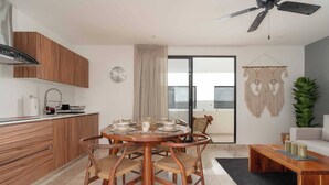 A modern kitchen with wooden cabinets, a dining table with chairs, a ceiling fan, and a sliding glass door leading to a balcony. - Beautiful and Comfortable, 1 Bedroom! The Best in Zama! (Tulum)
