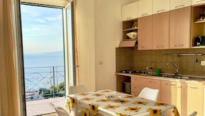 A dining area with a table covered in a sunflower tablecloth, white chairs, and a view of the sea through a large window. - 🏖️ Vacation by the sea: panoramic balcony in Vico Equense, near Sorrento (Vico Equense)