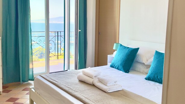 A bedroom with a bed, a view of the sea through a sliding door, and a balcony with a railing. - 🏖️ Vacation by the sea: panoramic balcony in Vico Equense, near Sorrento (Vico Equense)