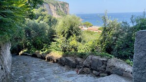 A stone pathway leading to a cliff overlooking a coastal area with buildings and greenery. - 🏖️ Vacation by the sea: panoramic balcony in Vico Equense, near Sorrento (Vico Equense)