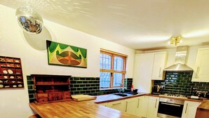 A modern kitchen with a wooden island, bar stools, a built-in oven, and a window with blinds.